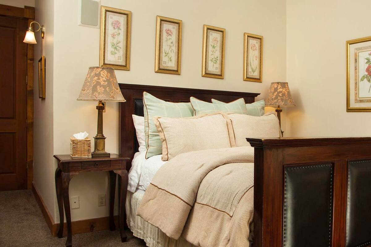 A neatly arranged bedroom with a bed, bedside tables, a wooden headboard, and floral wall art.