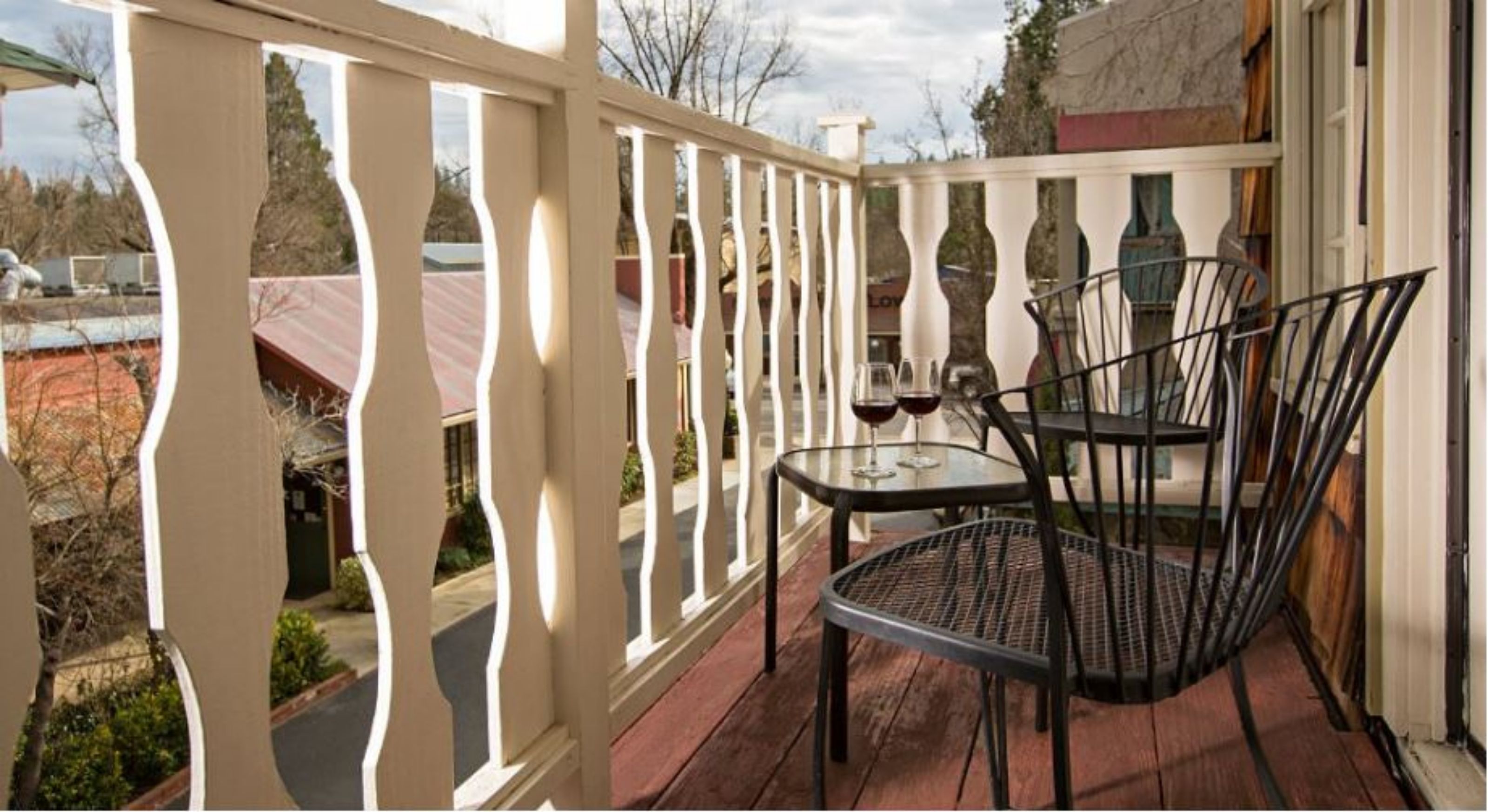 A covered outdoor area with a table and chairs, a white railing, and a view of the street.