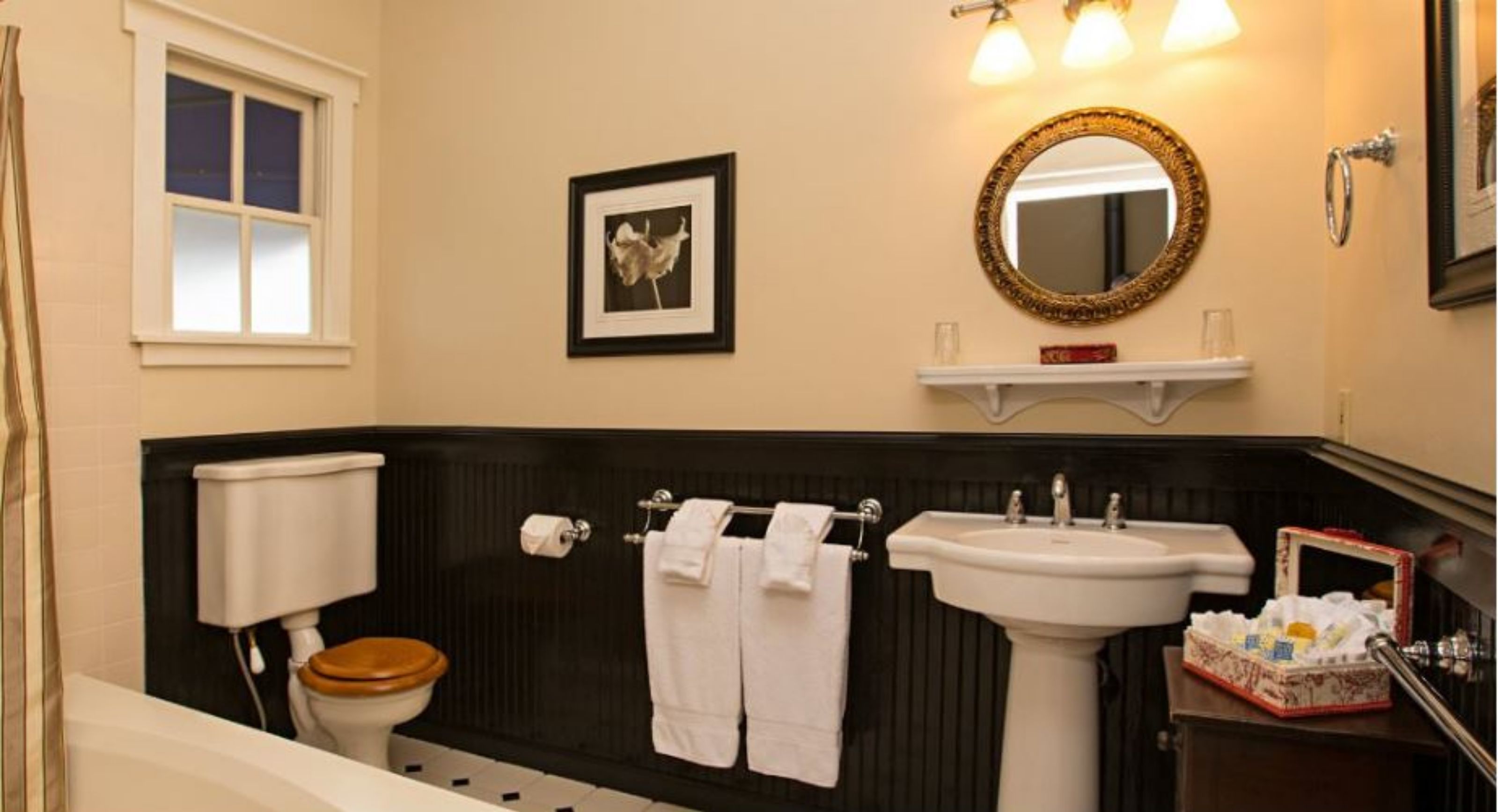 A bathroom with a toilet, sink, and bathtub. There is a framed picture on the wall, a towel rack, and a mirror above the sink.