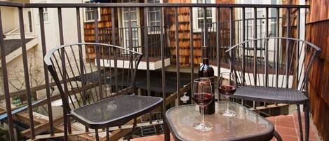 A small outdoor patio with two metal chairs and a table, a bottle of wine, and a glass on the table.