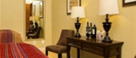 A hotel room with a bed, a desk with lamps, a chair, and a mirror.
