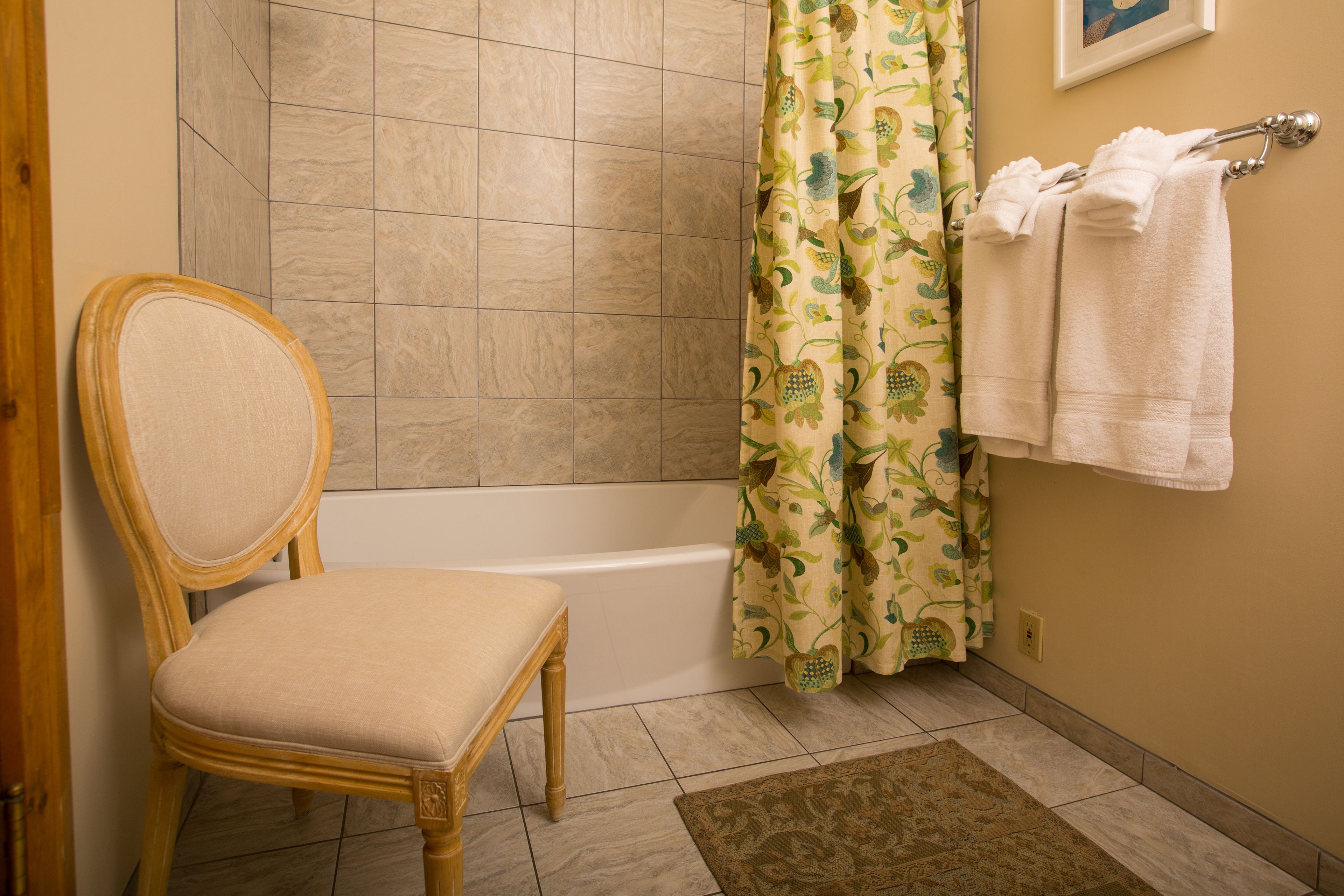 Un baño con una silla de madera, una bañera, una cortina de ducha y un perchero para toallas.