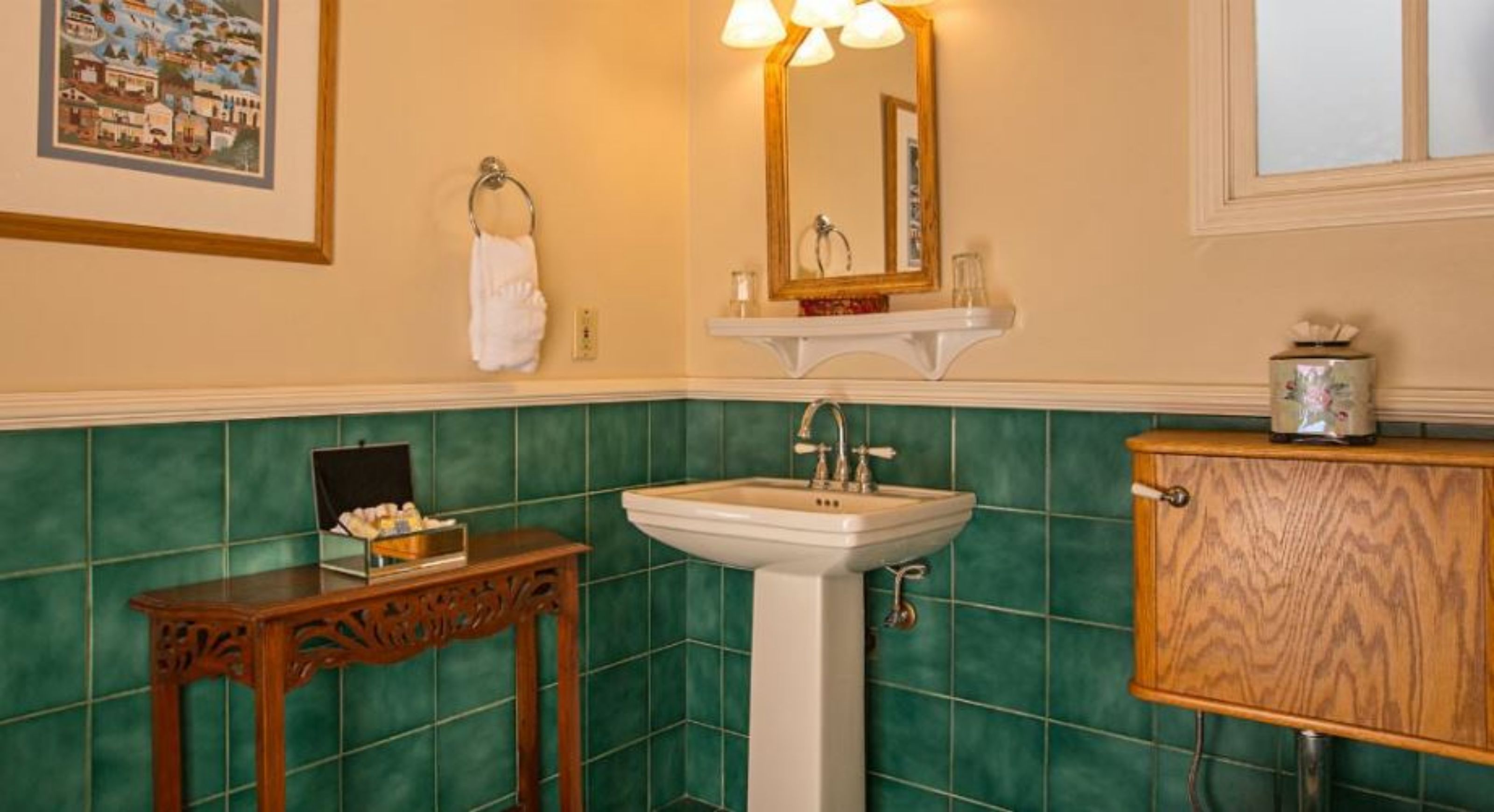 A bathroom with a white sink, green tiles, a wooden cabinet, and a framed picture on the wall.