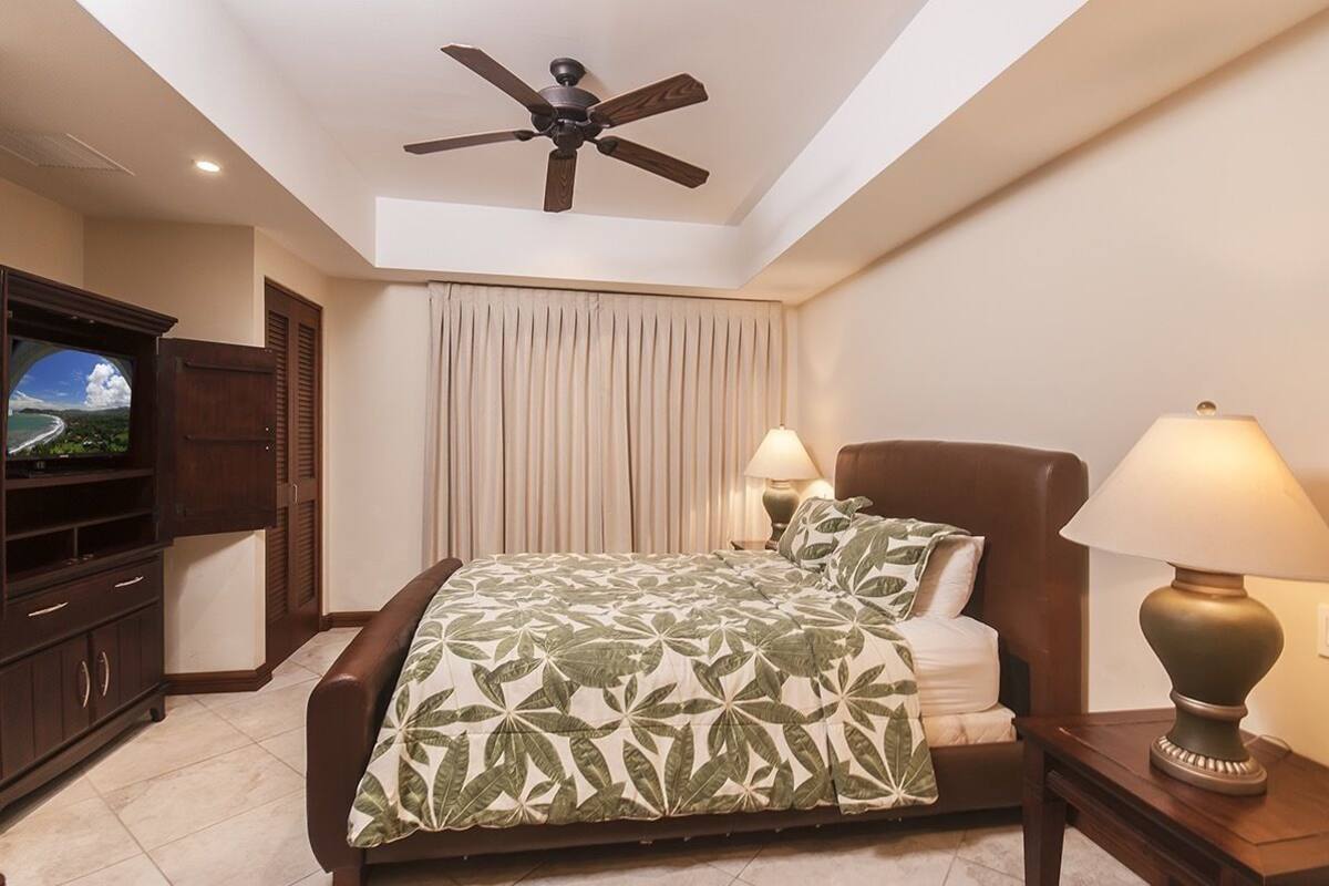 Ein Schlafzimmer mit Bett, Deckenventilator, Fernseher und Lampe.