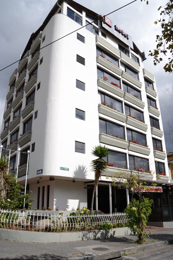 A multi-story hotel with balconies, a sign indicating the name, and a street sign.