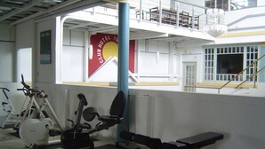Ein Fitnessraum mit Trainingsgeräten, einem roten Club Hotel ID Banner und Blick auf das Hotelgebäude.