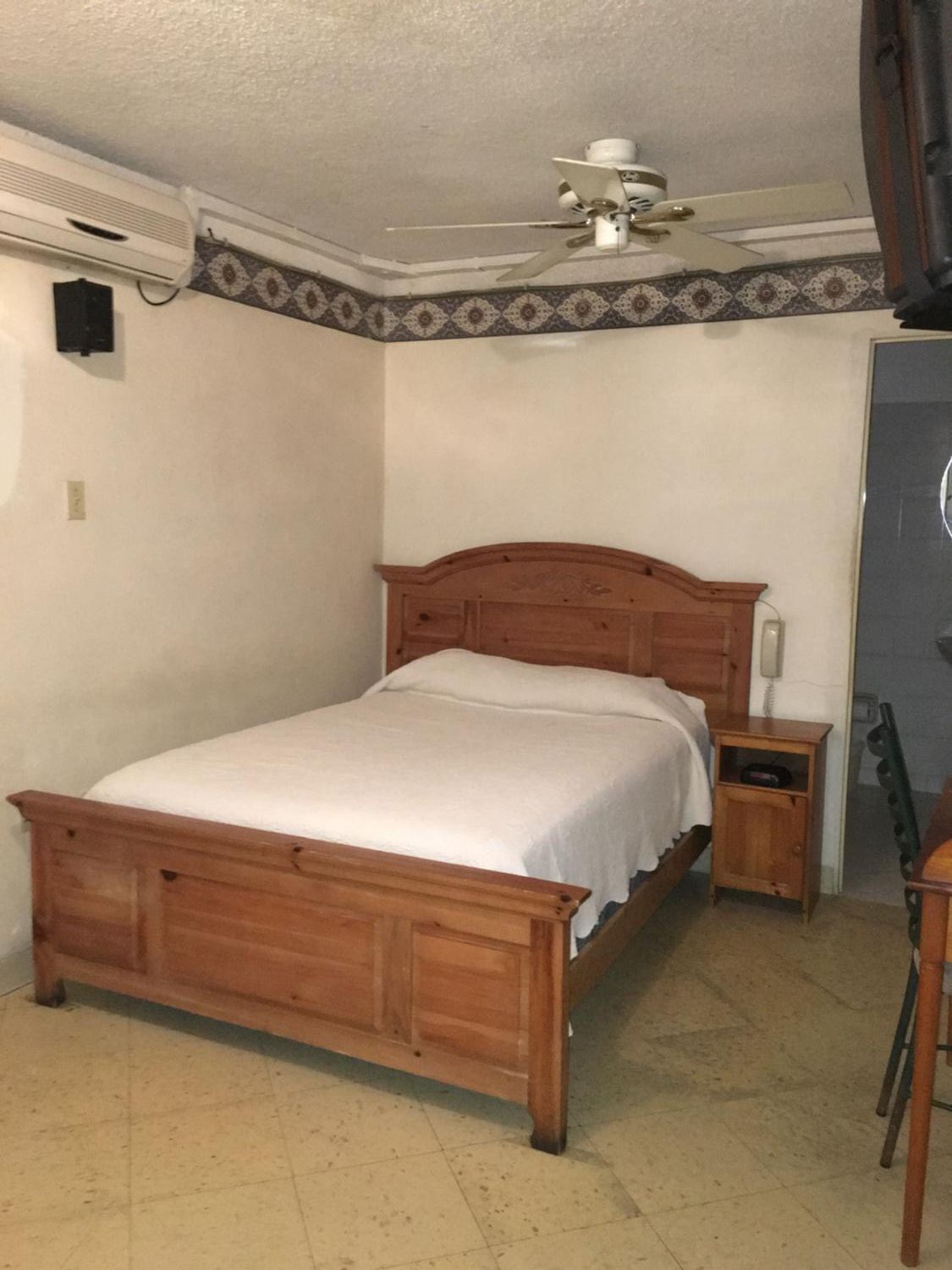 Un dormitorio con una cama de madera, una mesita de noche, un ventilador de techo y una puerta.