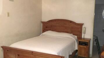 Un dormitorio con una cama de madera, una mesita de noche, un ventilador de techo y una puerta.