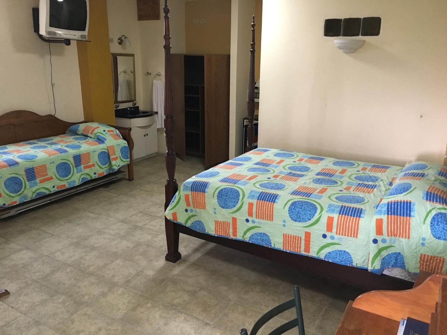 Una habitación con dos camas, un armario de madera, un televisor y un espejo.