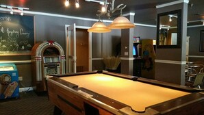 A pool table with overhead lighting, a jukebox, and a chalkboard with a message.
