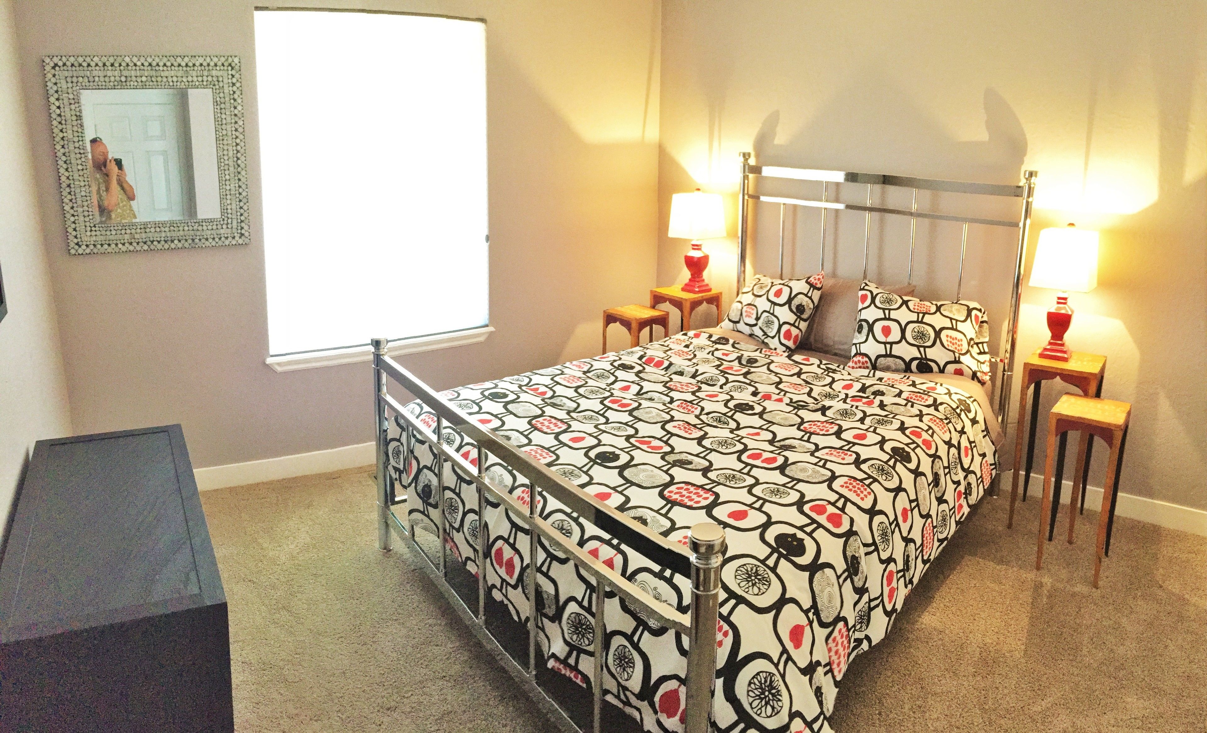 A bedroom with a bed, two bedside tables with lamps, a mirror, and a window.