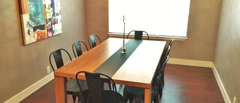 Een eethoek met een lange houten tafel, zes zwarte stoelen, een kroonluchter en een groot raam.