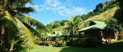Un resort tropical con varias cabañas de techo verde, rodeado de exuberante follaje y palmeras.