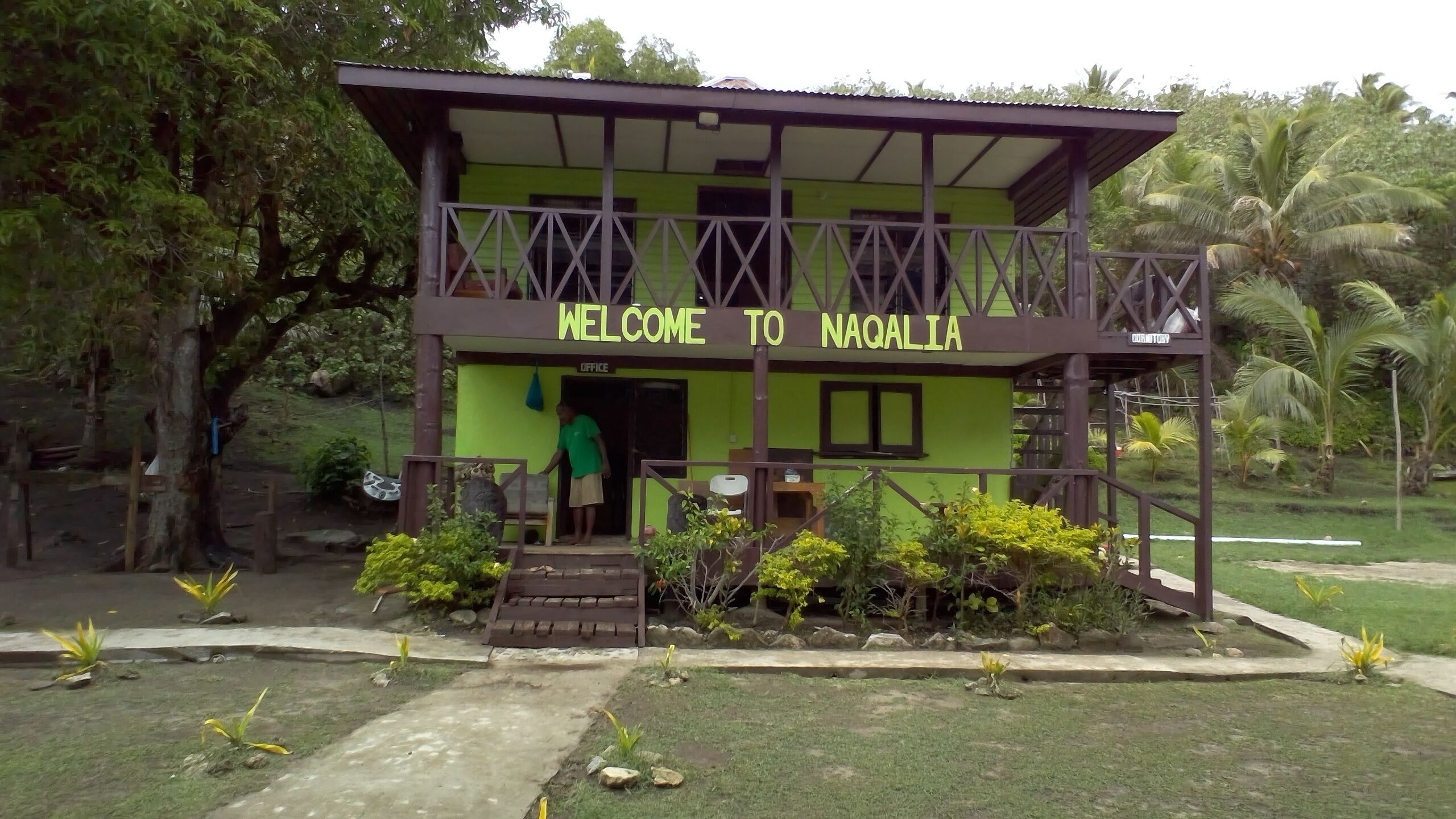 A building with a sign reading "WELCOME TO NAGALIA" and a person standing at the entrance.