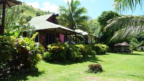 A tropical house with a thatched roof, surrounded by lush greenery and palm trees. - Naqalia Lodge (Wayasewa Island)