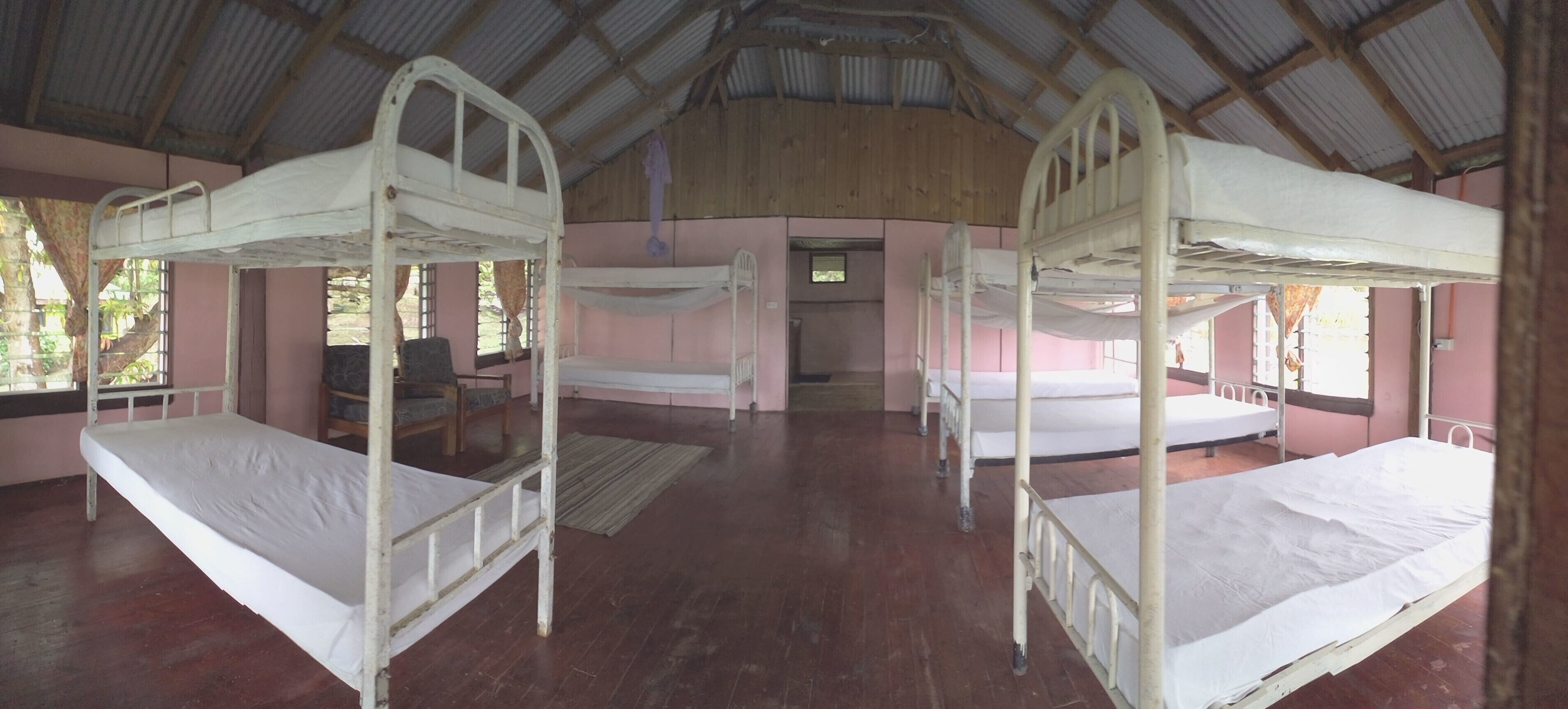 A room with bunk beds, wooden floors, and a pink wall.