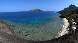 A coastal view with clear blue waters, a sandy beach, and a rocky shoreline. - Naqalia Lodge (Wayasewa Island)
