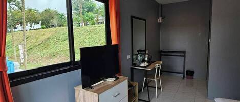 A modern hotel room with a large window, a TV on a wooden cabinet, a desk with a chair, and a bed.