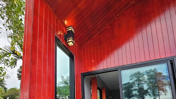 Un edificio moderno con fachada roja, amplios ventanales de vidrio y un interior visible con un escritorio y una silla.