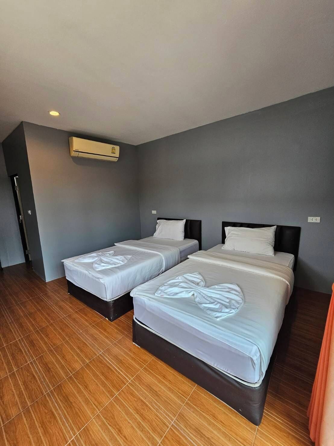 Una habitación de hotel con dos camas, piso de madera y un equipo de aire acondicionado en la pared.