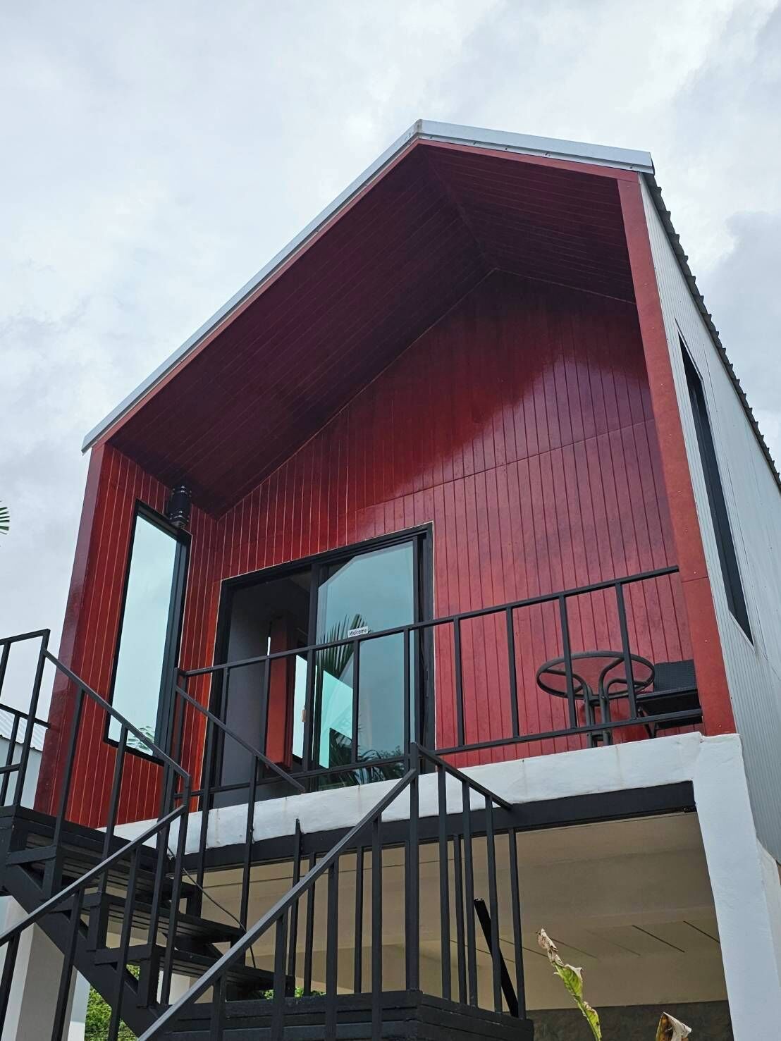 Un edificio moderno con fachada roja, un balcón con barandilla metálica y una escalera que conduce a la entrada.