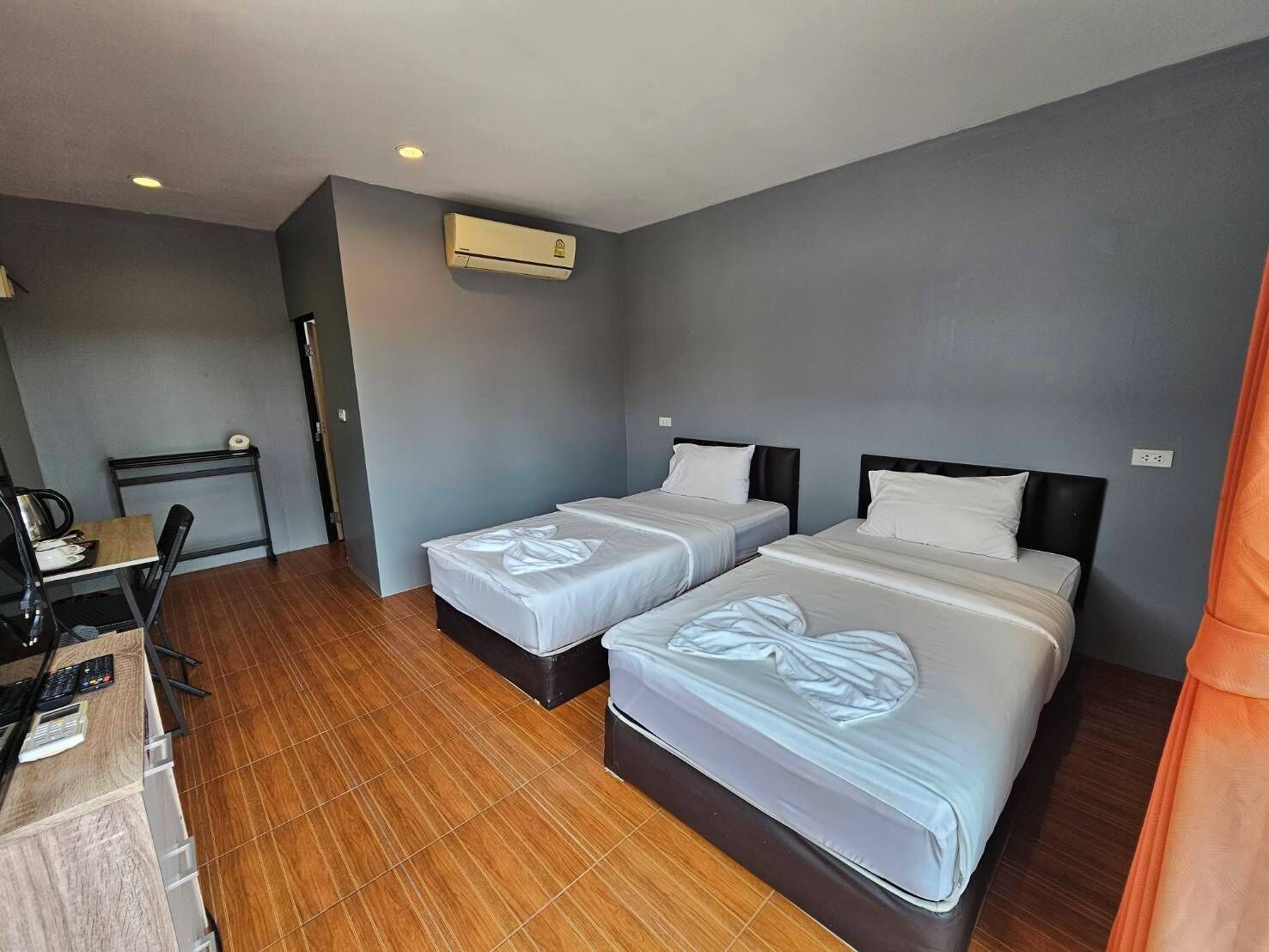 A hotel room with two beds, a desk with a chair, and an air conditioning unit.