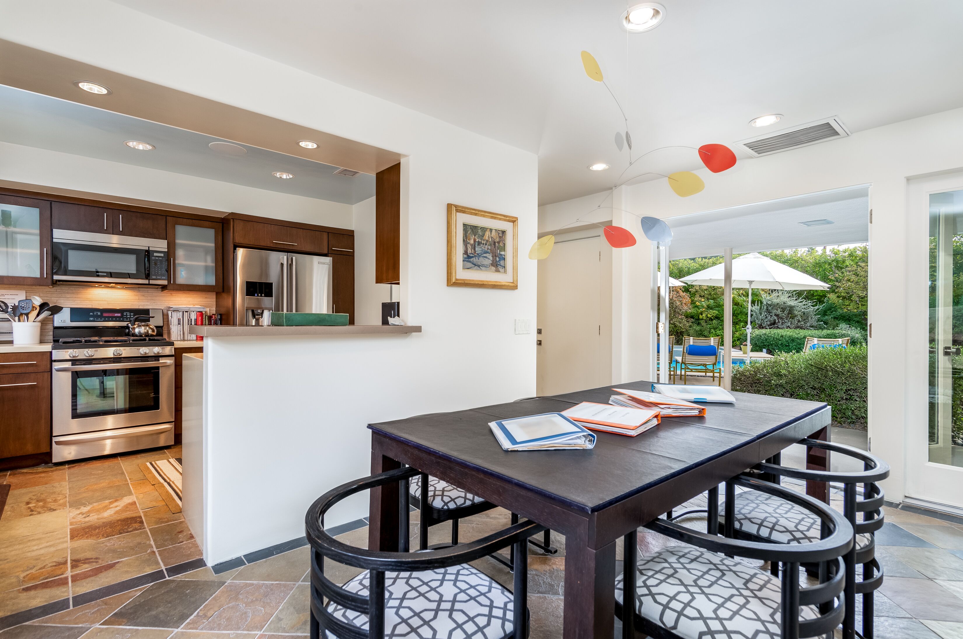 A modern kitchen with stainless steel appliances, a dining area with a table and chairs, and a view of a garden through a glass door.