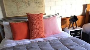 A neatly made bed with a grey quilt, two white towels, and two pillows in orange and pink.