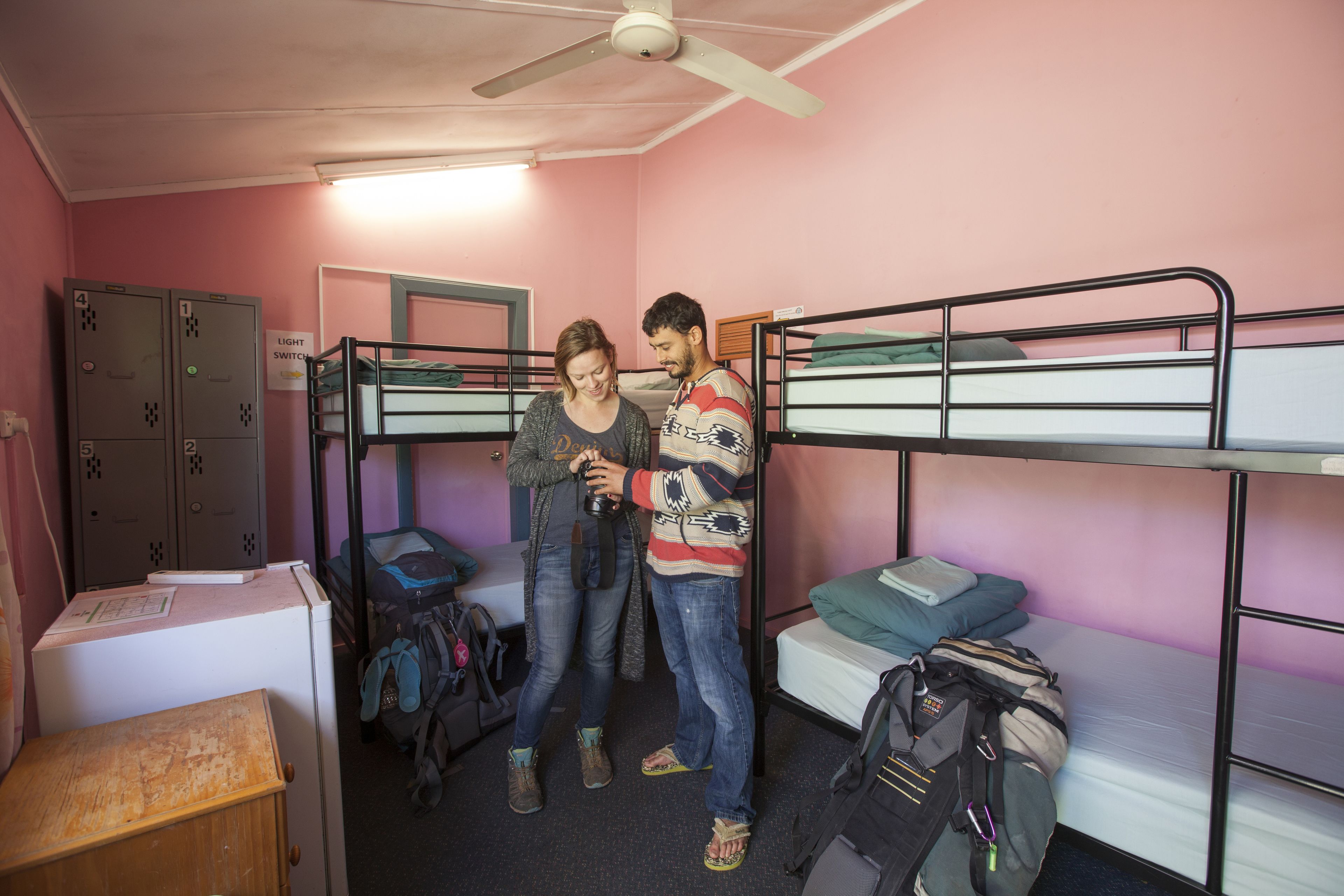 A dormitory room with bunk beds, lockers, and a refrigerator.