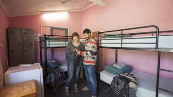 A dormitory room with bunk beds, lockers, and a refrigerator.