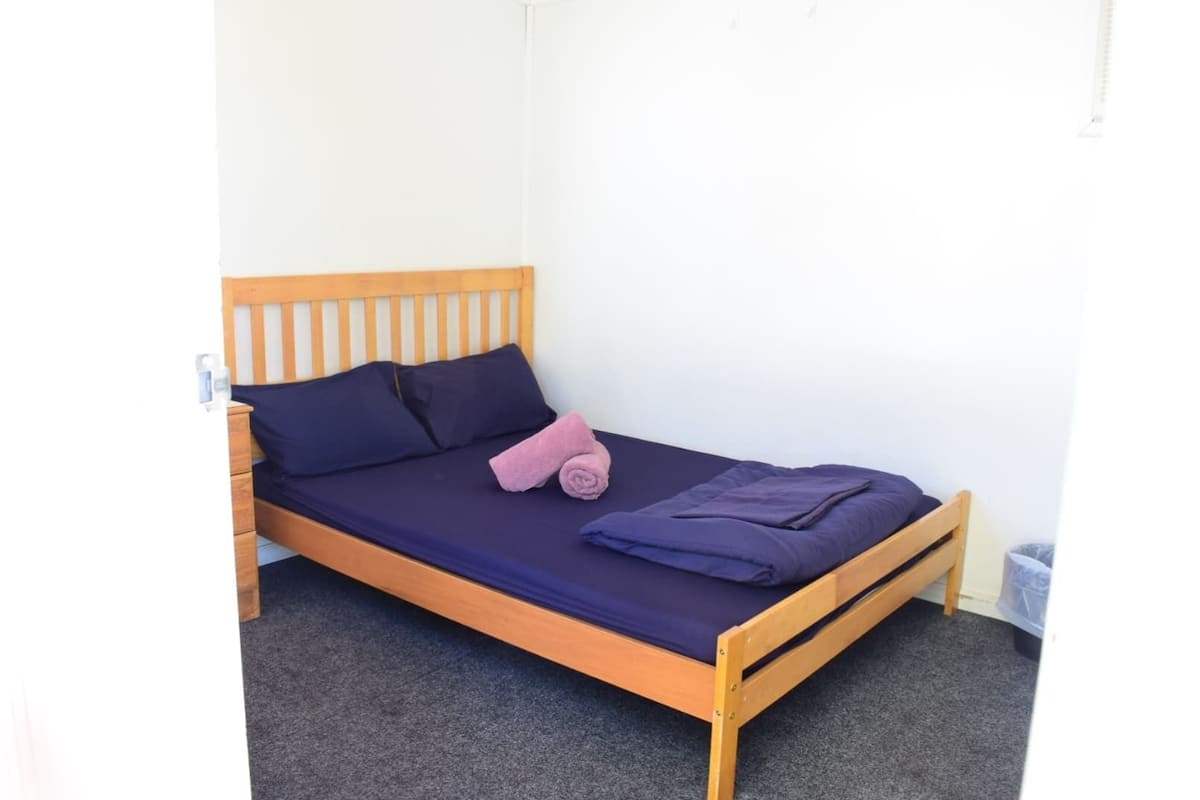 Uma cama de solteiro com estrutura de madeira, roupa de cama azul escura e uma toalha rosa.