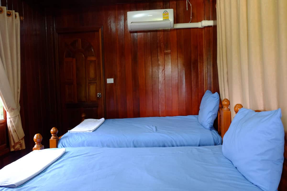 Ein Zimmer mit zwei Betten, Holz-Kopfteilen, einem fenster mit Vorhängen und einer Klimaanlage an der Wand.