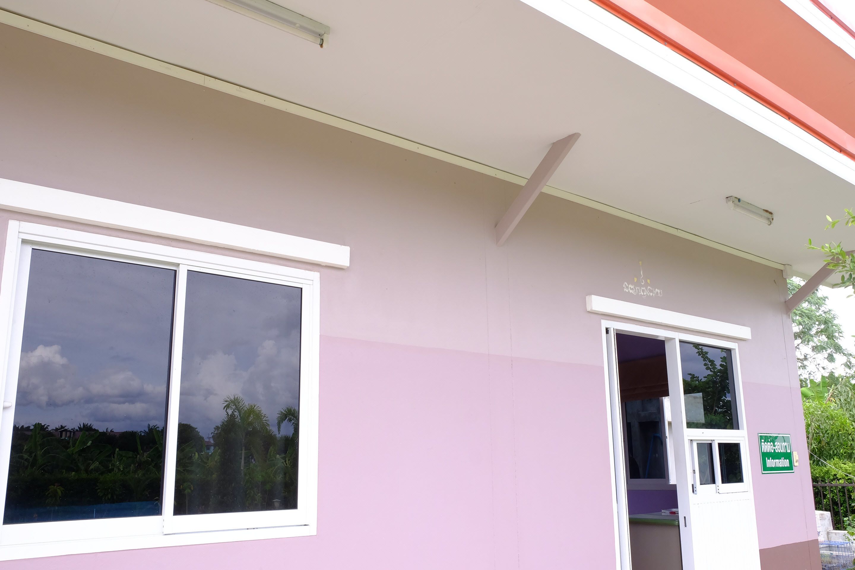 Un edificio con fachada rosa, marco de ventana blanco y un letrero verde que indica un punto de información.