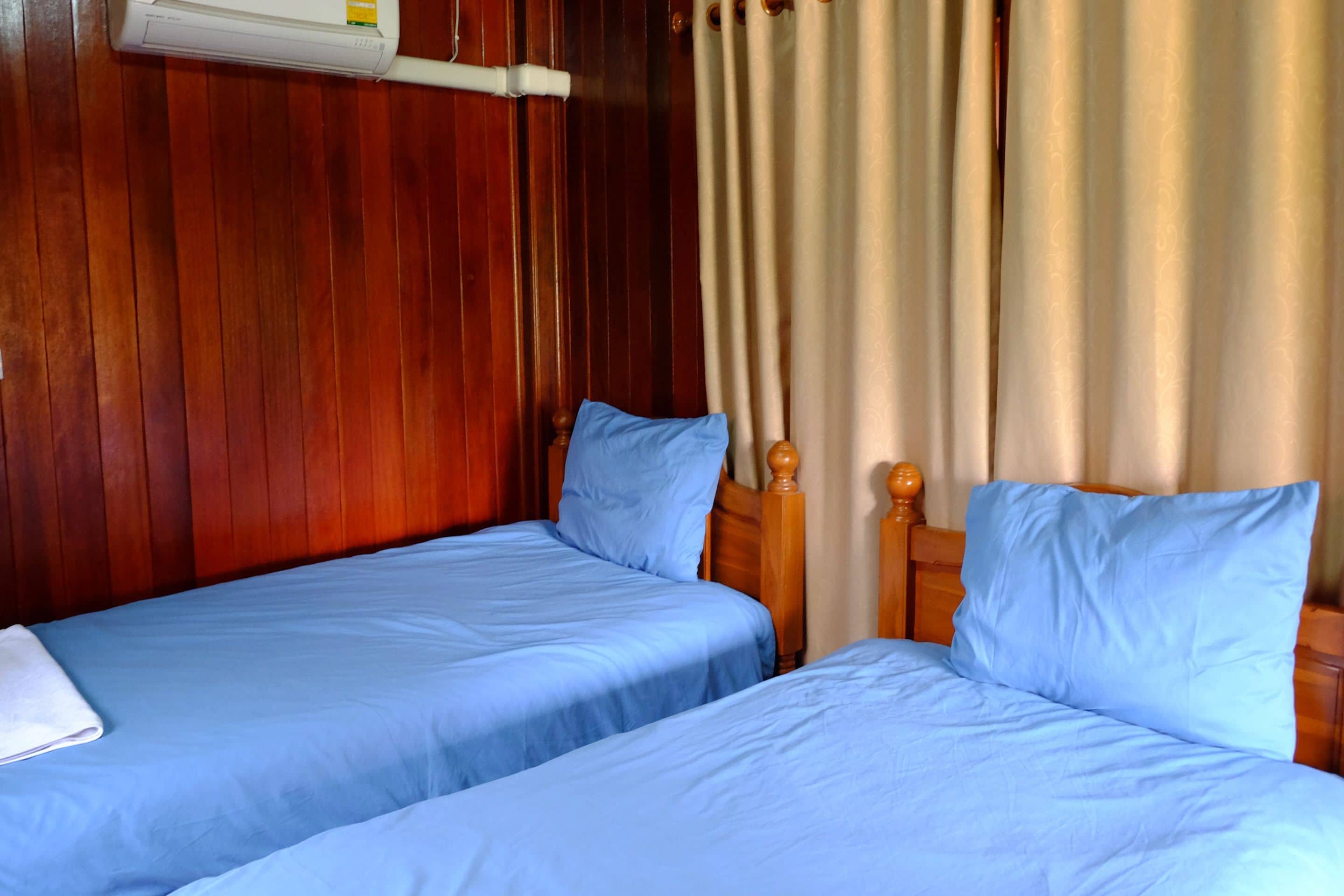 Een kamer met twee enkele bedden, houten hoofdborden en een raam met gordijnen.