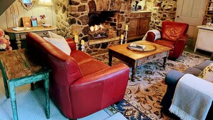 Un salon chaleureux avec une cheminée en pierre, des canapés en cuir, une table basse en bois et un lustre.