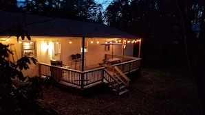 Una cabaña de madera con terraza, luces cálidas y una mesa de picnic.