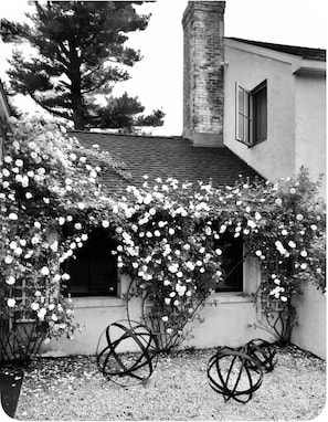 Un bâtiment doté d’un porche abrité, d’une cheminée et d’un arbre en arrière-plan.