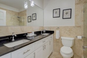 A bathroom with a large mirror, two framed pictures, a sink, a toilet, and a shower.