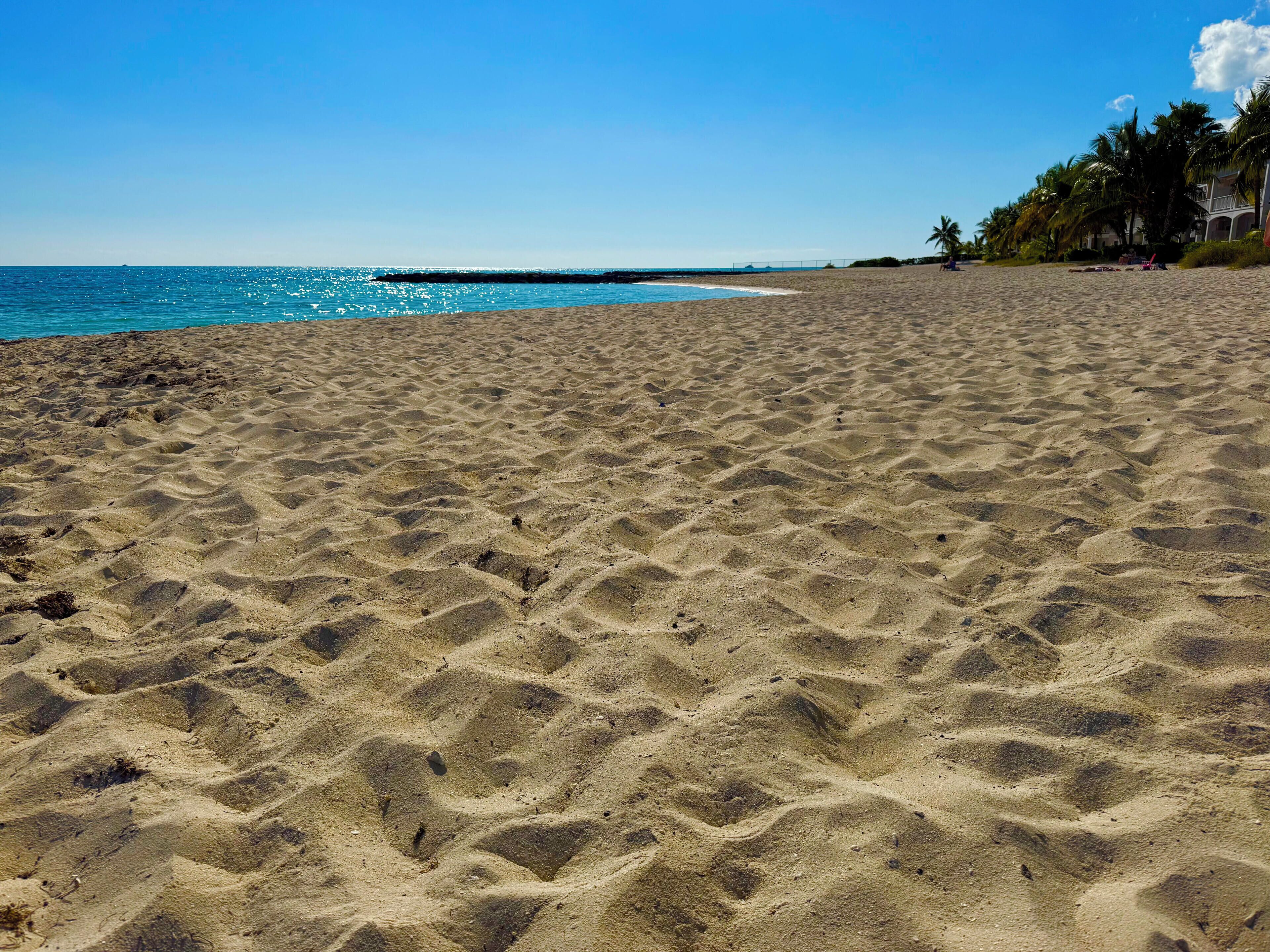 A sandy beach with a clear blue sky and calm sea.