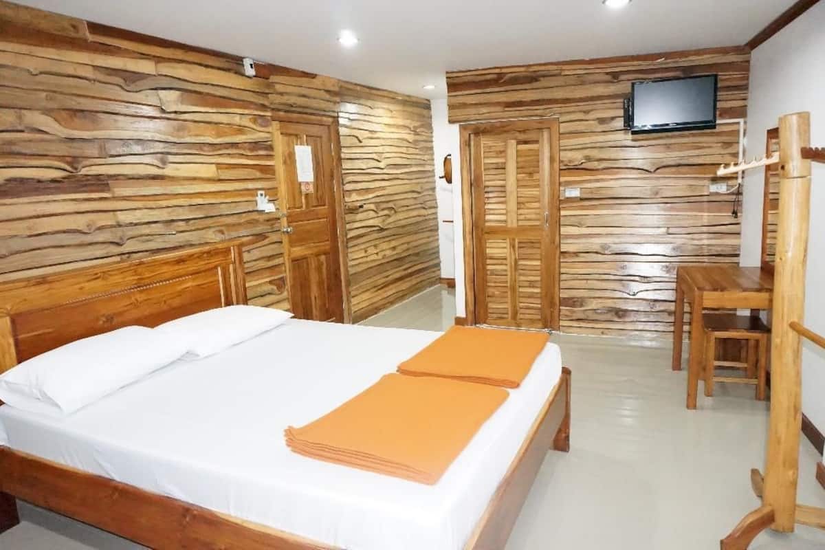 A bedroom with a wooden headboard, a bed with white and orange bedding, a wooden desk with a chair, and a television mounted on the wall.