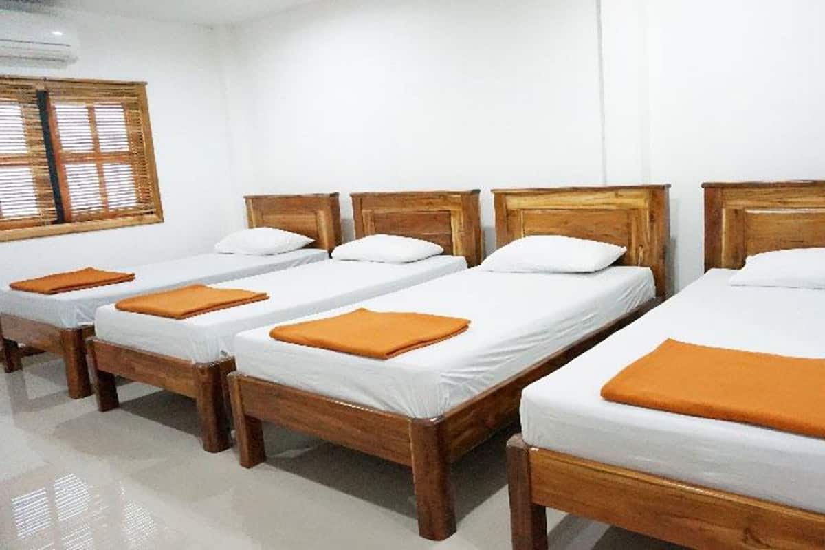 Four single beds with wooden frames and white bedding, arranged in a row with orange throw pillows.