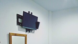 Une petite pièce avec une chaise en bois, une petite table ronde avec une chaise, un téléviseur fixé au mur et un miroir.