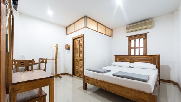 Une chambre à coucher avec un lit en bois, un bureau avec des chaises, une armoire et une fenêtre avec des stores.