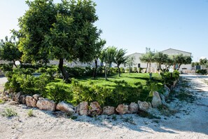 Un jardín ajardinado con diversos árboles y arbustos, un sendero de grava y un edificio al fondo.