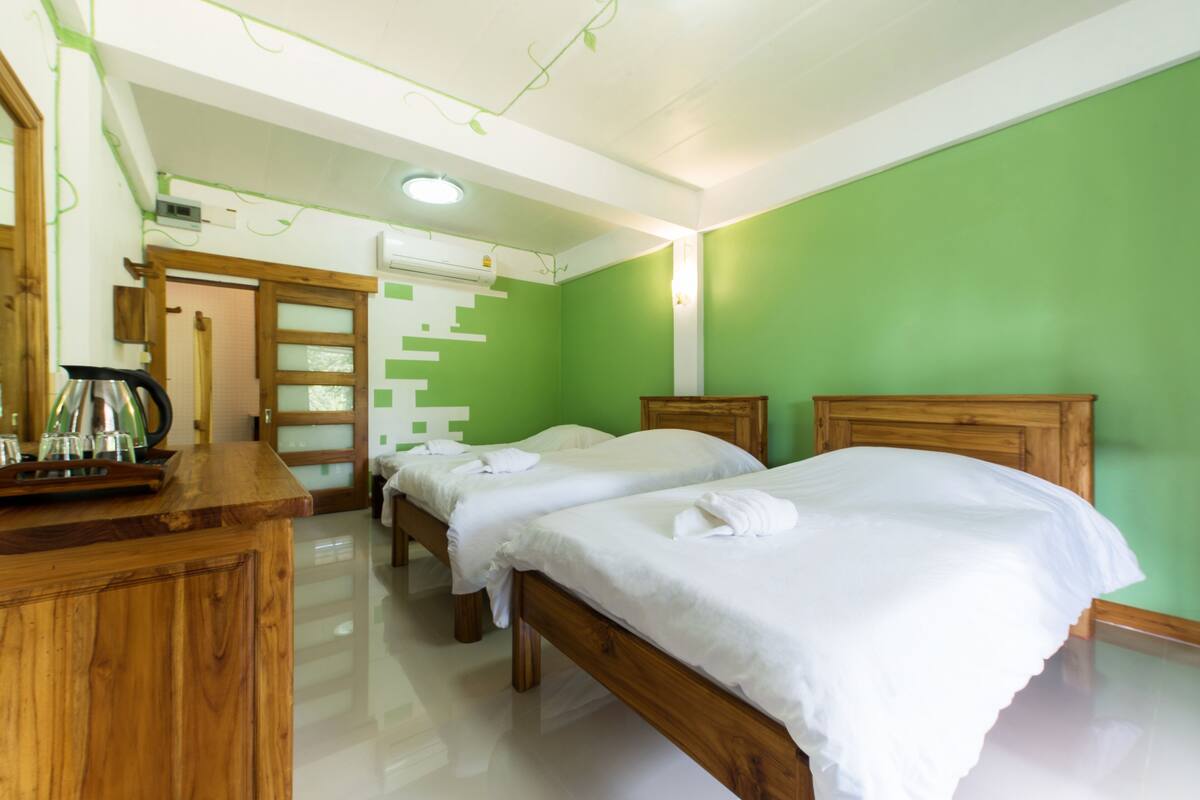A hotel room with two wooden beds, a wooden dresser, a staircase, and a green wall.