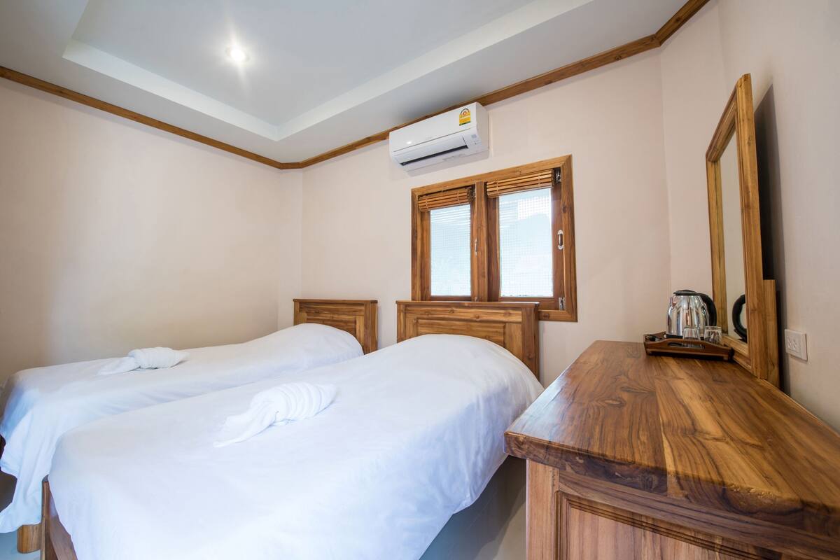 A hotel room with two beds, a wooden dresser, a mirror, and an air conditioning unit.