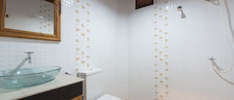 A bathroom with a glass sink, white toilet, and shower.