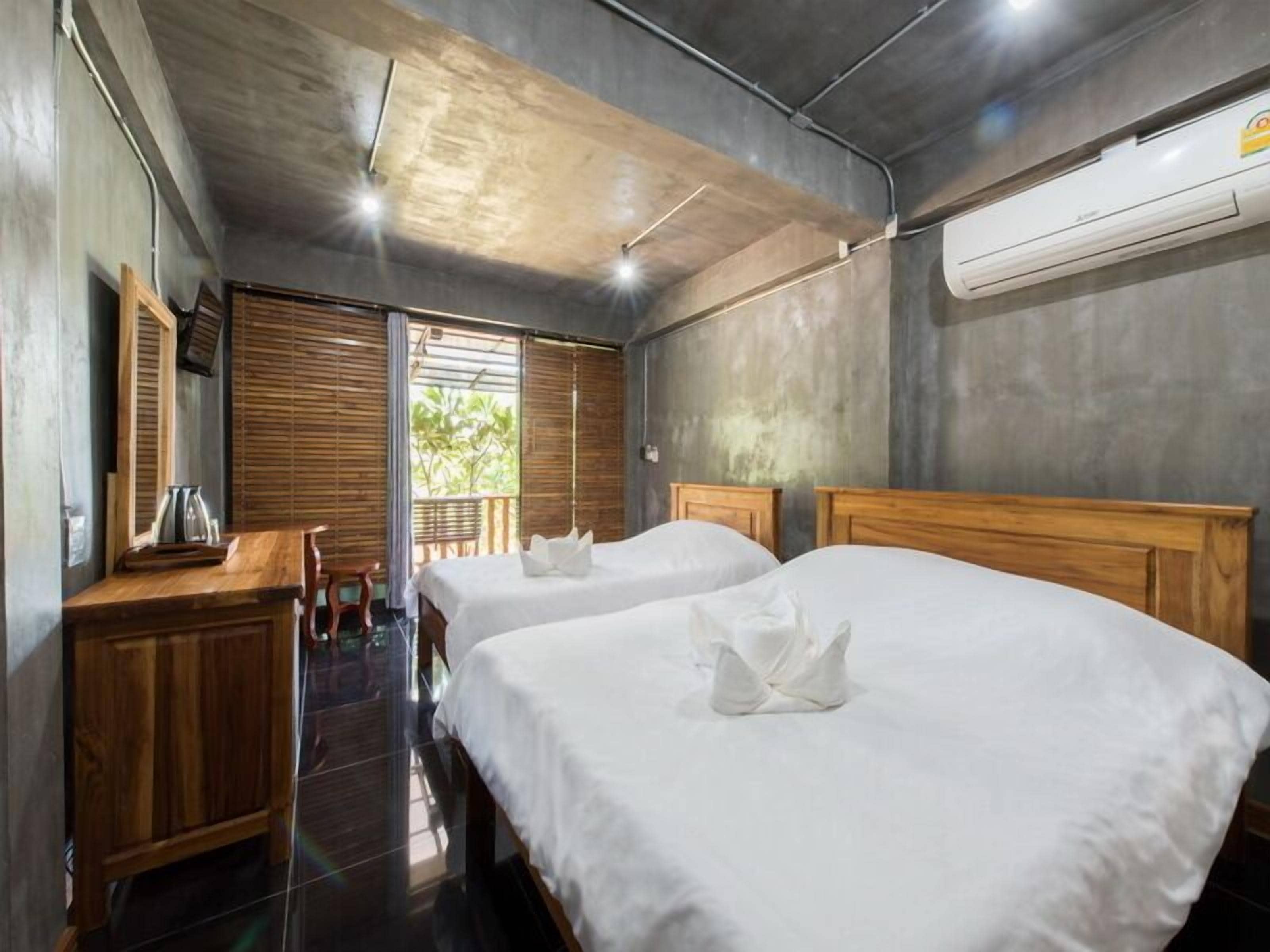 A hotel room with two beds, a wooden desk, a chair, and an air conditioning unit.
