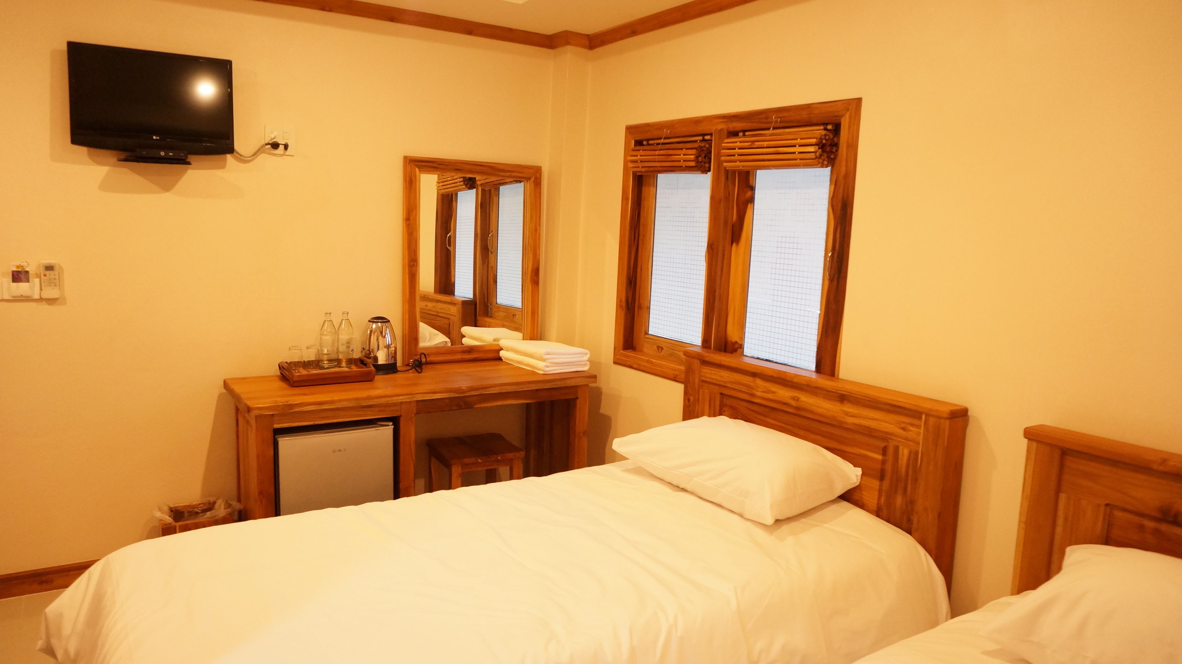 A hotel room with two beds, a desk with a mirror, a television, and a window with wooden shutters.