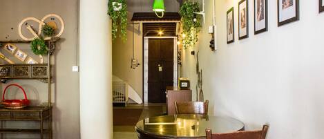Un comedor con una mesa redonda, sillas y plantas colgantes. Una escalera conduce a otra habitación.